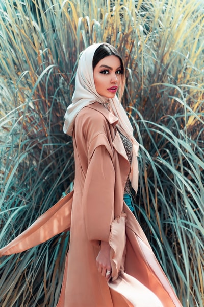 During the day, a woman wearing a brown scarf standing next to the green plants